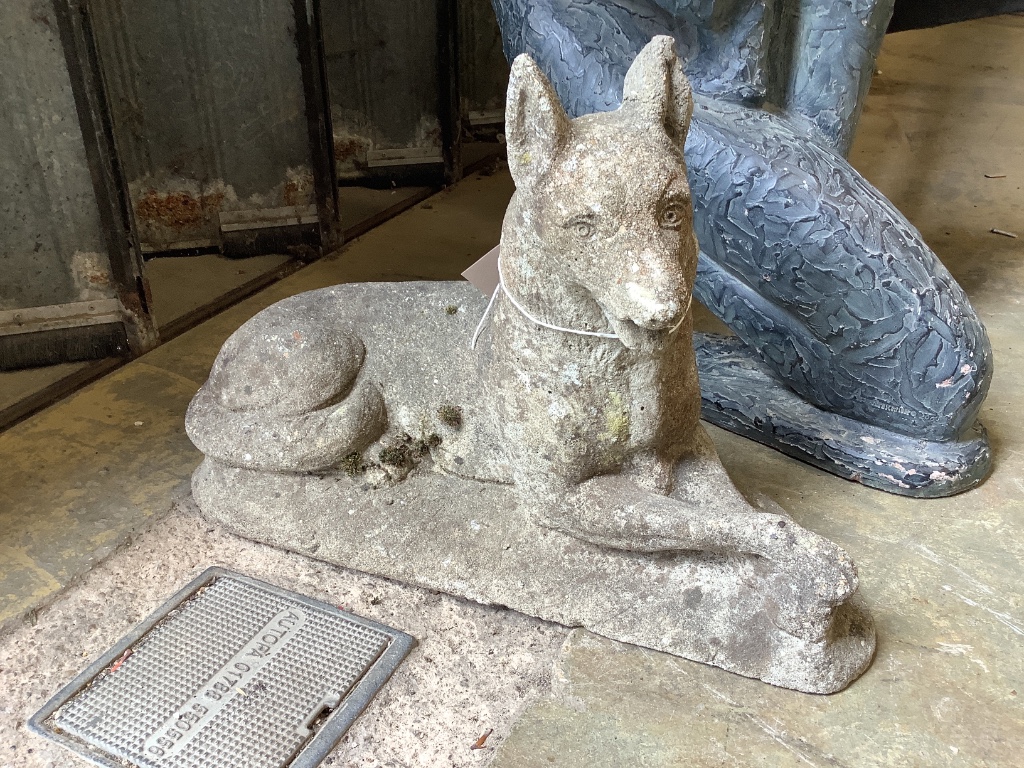 A reconstituted stone garden ornament of a recumbent German Shepherd dog, length 50cm